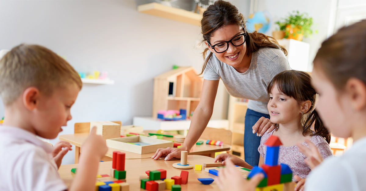 Een medewerkster in de kinderopvang speelt samen met drie kinderen met Duplo.